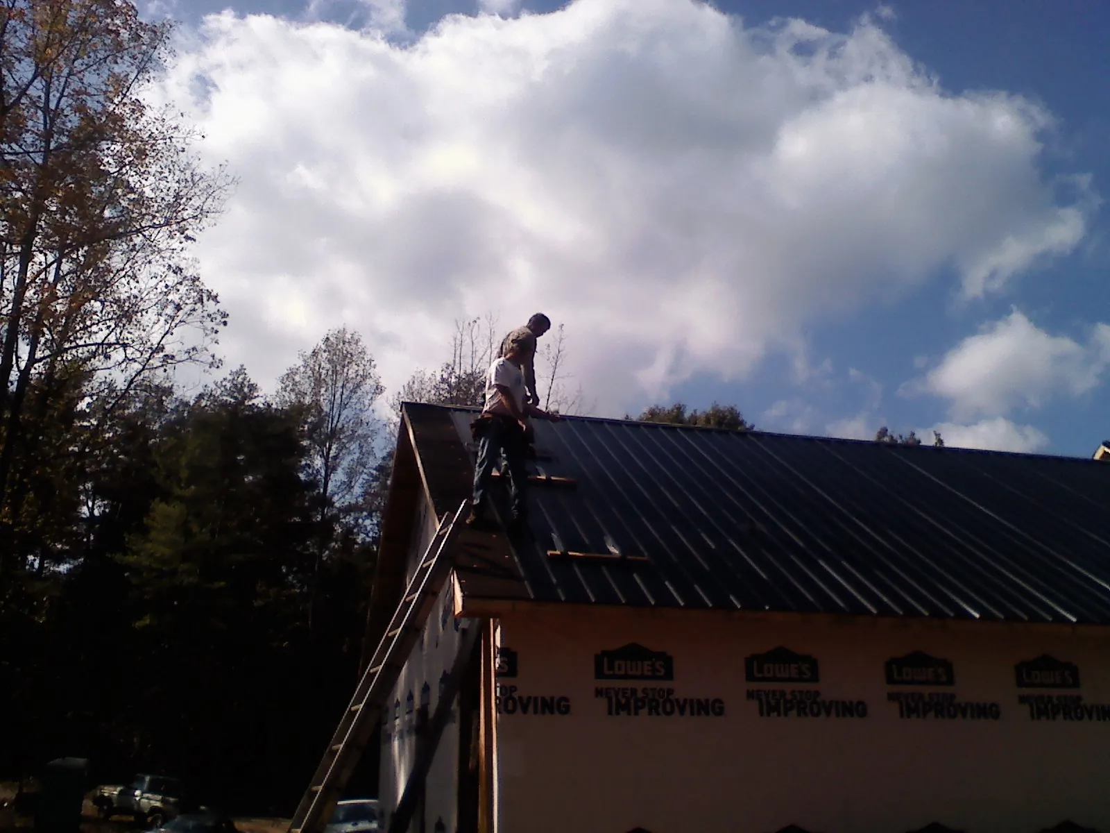 Roofer fastening dark metal panels high against a cloudy sky, from a Roof Inspection job in Columbus