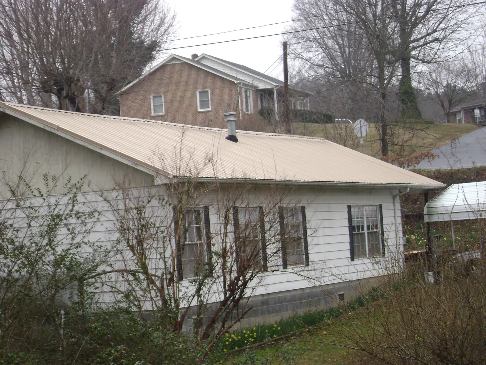 Tan metal roof on a white sided house set into a hillside — Commercial Roofing by Roofing Brothers in Columbus
